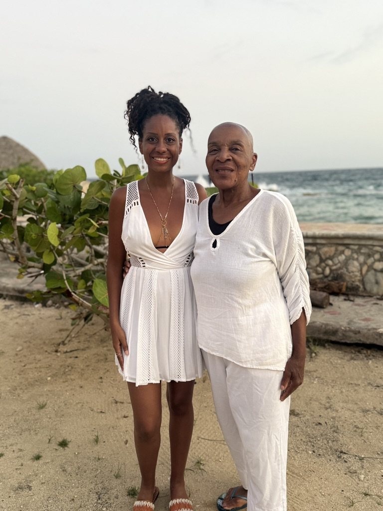 Cheyennis Doom and Linda James Myers, Ph.D., both dressed in white, standing together on a beach at dusk