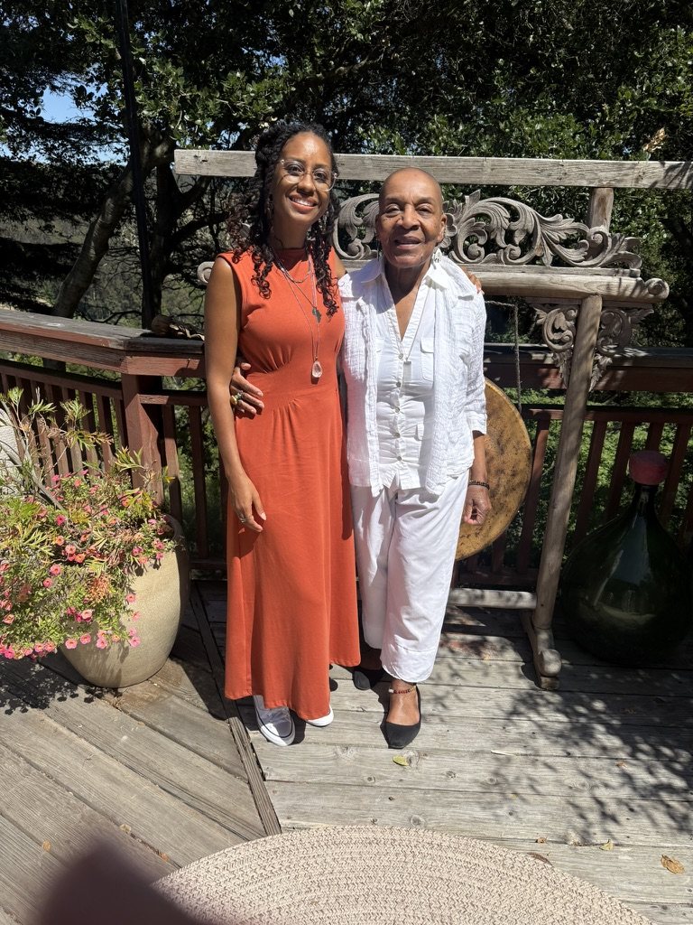 Cheyennis Doom and Linda James Myers, Ph.D. smiling together on a sunny wooden deck